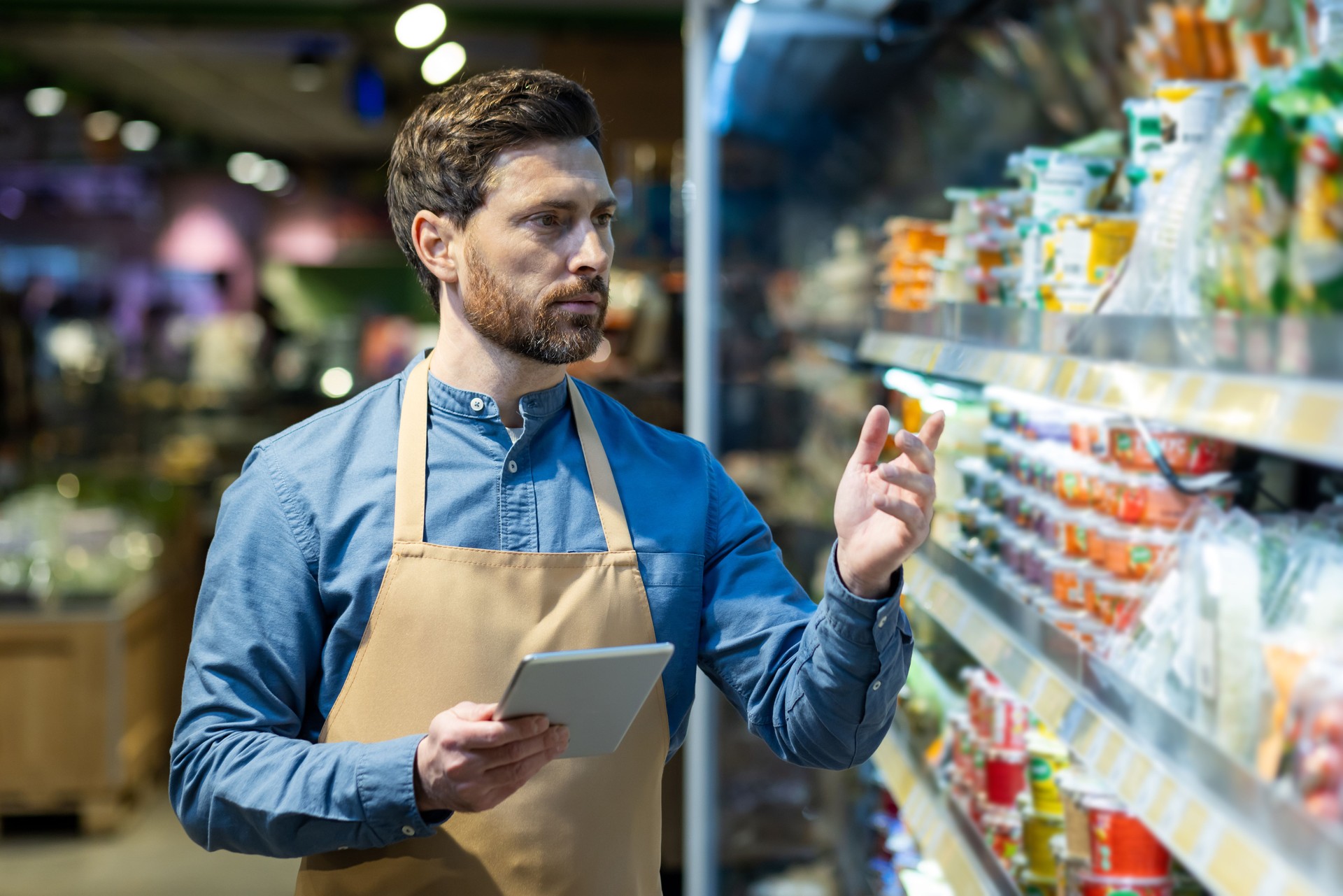 Supermarket employee using tablet to manage inventory while checking products on shelves